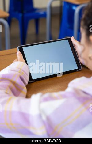 African American youth female student sitting at school desk holding tablet in case, blue chairs Stock Photo