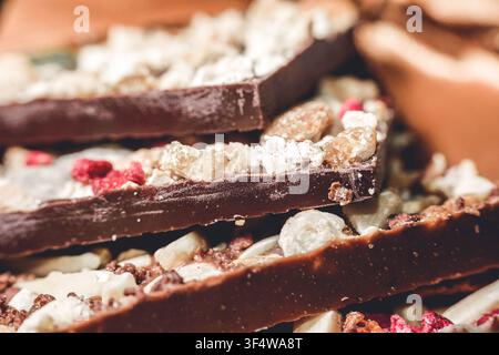 Close-up shot of stacked dark chocolate bars embedded with whole nuts dried fruit and powdered inclusions presented on a wooden surface Stock Photo