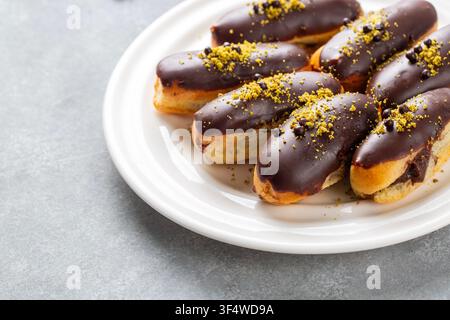 Chocolate eclairs topped with chopped pistachio and chocolate crisps served on white plate Stock Photo