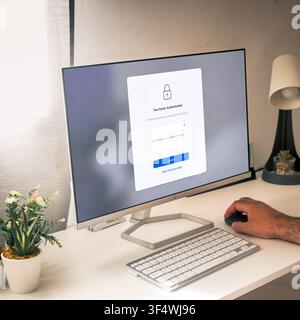 Hand uses a mouse beside a desktop monitor showing a two-factor authentication form with verification code fields in a bright workspace. Stock Photo