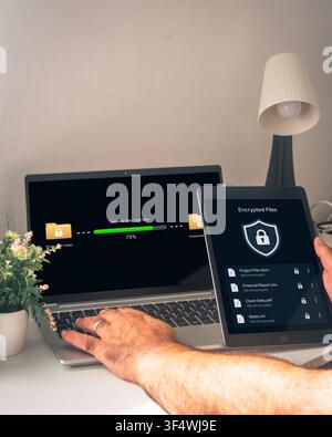 Hands use a laptop beside a tablet showing encrypted files while a secure file transfer progresses between protected folders on screen. Stock Photo