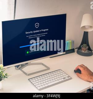 Hand uses a mouse while a desktop monitor shows a security update and patch installation progress bar in a bright modern workspace. Stock Photo