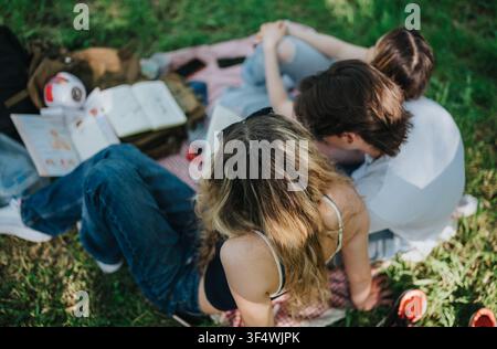 Teen friends sitting on a picnic blanket outdoors reading and relaxing during a casual hangout Stock Photo