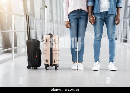 Travelling Together. Black Couple Holding Hands While Standing In Airport Corridor, Cropped Stock Photo