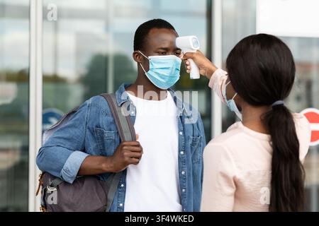 Airport Worker Checking Black Male Passenger Temperature With Electronic Thermometer After Arrival Stock Photo