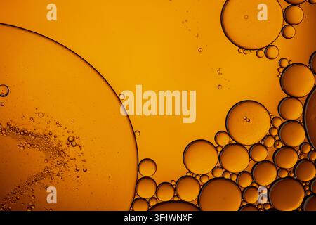 Golden oil drops creating abstract circles and bubbles on a warm liquid background Stock Photo