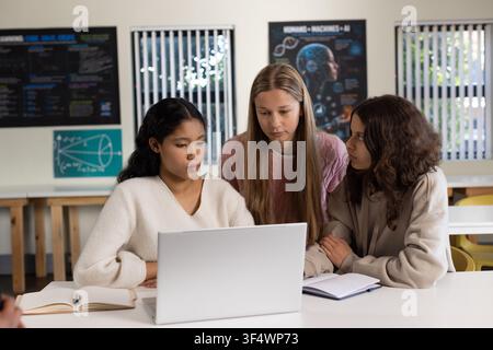 Diverse teenage female students studying together around silver laptop in classroom with open book Stock Photo