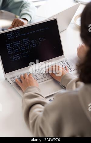 Youth students coding together at study table in library with silver laptop showing code Stock Photo