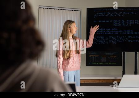 Youth female students wearing pink knit presenting code on screen gesturing in class with laptop Stock Photo