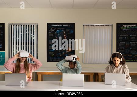 Diverse teenage students using white VR headsets and working on silver laptops at tech lab Stock Photo