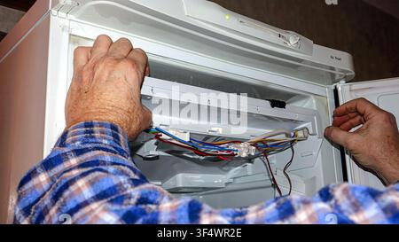 A skilled technician examines and repairs the intricate wiring of a refrigerator in a modern kitchen, ensuring proper functionality and efficiency. Stock Photo