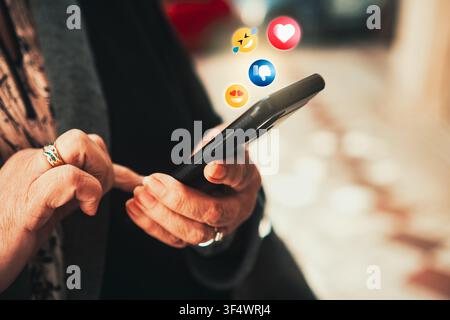 Social media reactions concept, senior woman using smartphone with emoji icons floating above screen. Social media marketing,technology. Stock Photo