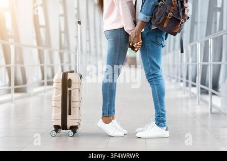 Romantic black couple travelling together, holding hands at airport, side view Stock Photo