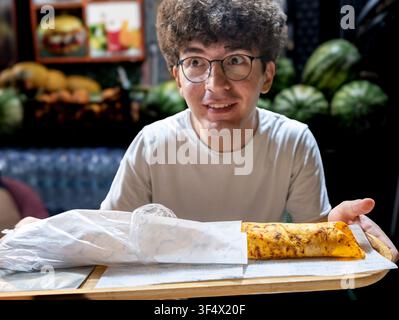 Istanbul, turkey. August 2, 2025. Young man holding a tray with two traditional turkish durum wraps, ready to eat street food in istanbul, turkey Stock Photo