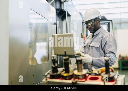 Professional engineer black male worker control operate CNC Machine high precision steel milling machine in heavy industry metal factory Stock Photo