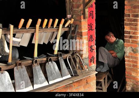 A man resting in a traditional blacksmith workshop in Taiwan with hand tools on display Stock Photo