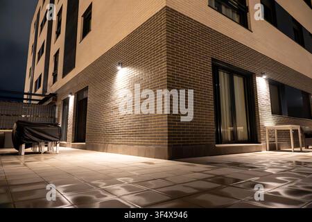 Building wall lights creating reflections on wet tiled ground of residential terrace Stock Photo