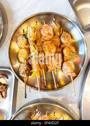 Grilled shrimp skewers served on a round golden metal plate at a traditional Korean BBQ restaurant. Stock Photo