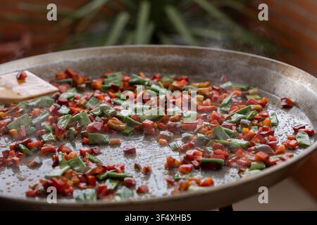 Sauteing fresh vegetables in paella pan for cooking Stock Photo