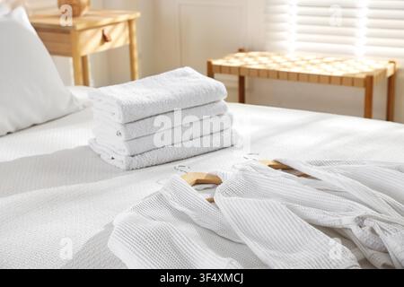 Clean bathrobes and towels on bed indoors Stock Photo
