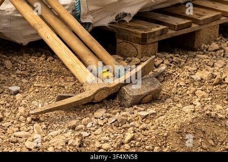 Close-up of pickaxes and digging tools resting on gravel at a construction site. Ideal for construction, excavation and manual labor concepts. Stock Photo