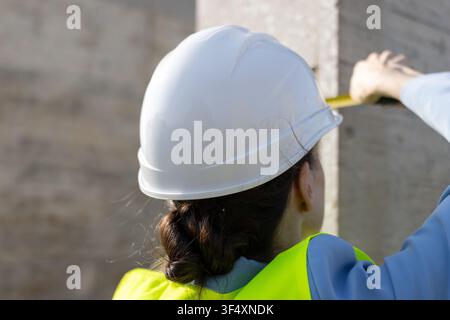 Woman engineer in hard hat and safety vest measuring concrete column on construction site Stock Photo