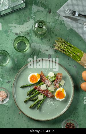 Asparagus spears served with crispy bacon, soft boiled eggs, and parmesan cheese on a green plate Stock Photo