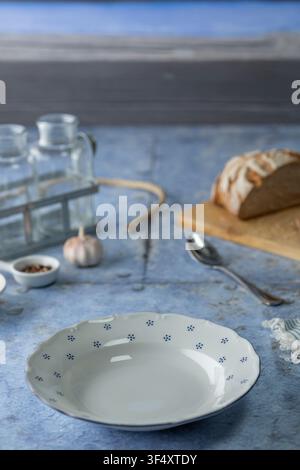 Empty white plate with blue pattern on a rustic blue wooden background with bread, garlic, and bottles Stock Photo