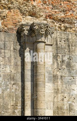 Ancient stone column featuring a sculpted capital against weathered brickwork and stone Stock Photo