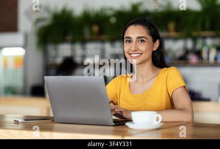 Cheerful female student using laptop at cafe Stock Photo