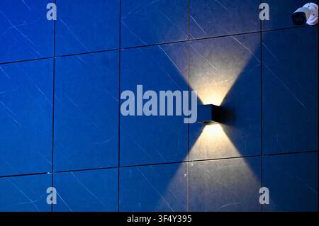 wall-mounted light fixture illuminates modern indoor building with clean blue and white tiles close-up side view, creating a sleek and contemporary atmosphere in the space.........m. Stock Photo