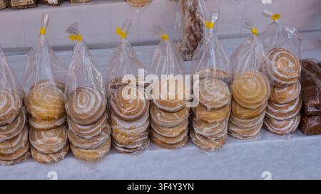Stacked round cookies in transparent bags displayed on a table at a market, showcasing various colors and textures of baked goods for sale Stock Photo