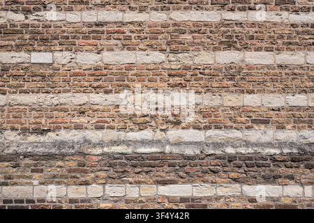 old masonry wall featuring alternating horizontal bands of reddish-brown clay bricks and lighter-colored ashlar stone blocks Stock Photo