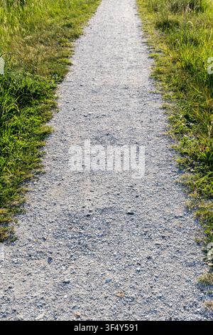 straight, narrow gravel path flanked on both sides by grass Stock Photo