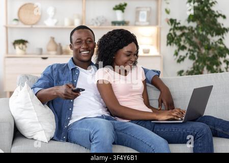 Young african american couple watching TV and using laptop Stock Photo