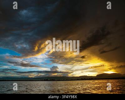 Stormy, cloudy sunset over Inle Lake in Myanmar, dramatic sky with dark rain clouds and warm evening light reflecting on the water around floating vil Stock Photo
