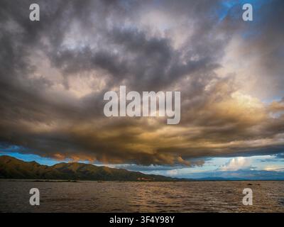 Stormy, cloudy sunset over Inle Lake in Myanmar, dramatic sky with dark rain clouds and warm evening light reflecting on the water around floating vil Stock Photo