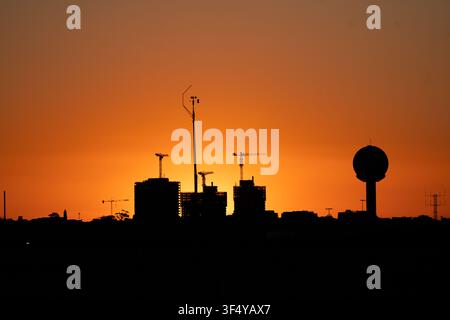 View of the Sydney Airport silhouette featuring construction cranes and a water tower against a vibrant orange sunset sky in Mascot, New South Wales, Stock Photo
