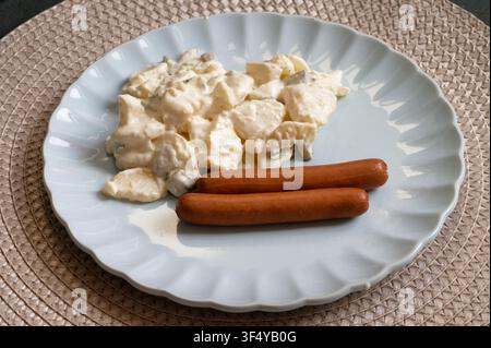 Creamy potato salad with mayo and spring onions served with two hot dogs on a plate. Traditional simple meal. Stock Photo