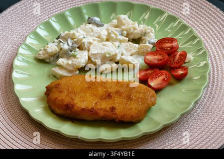 Golden brown breaded cutlet served with German potato salad and fresh sliced cherry tomatoes on a plate. Home-cooked food. Stock Photo