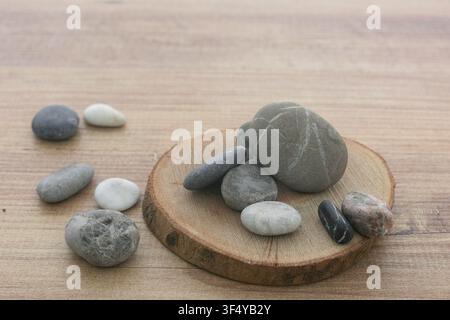 Natural sea pebbles pile on round wooden slice background. Stock Photo