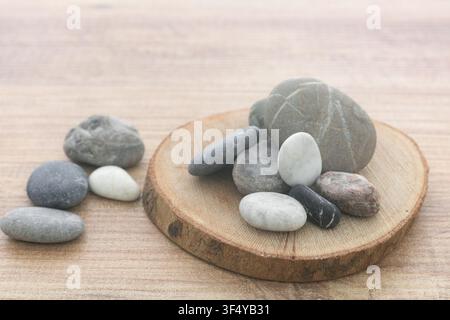 Natural sea pebbles pile on round wooden slice background. Stock Photo