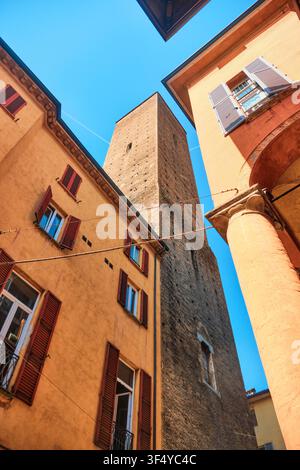 Bologna, Italy - May 2026: Low angle vertical view of historic medieval tower framed by colorful residential facades and portico column Stock Photo