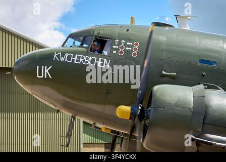 Close-up of Douglas C-47 Dakota "Kwicherbichen" showing nose art, mission markings, and pilot in the cockpit Stock Photo