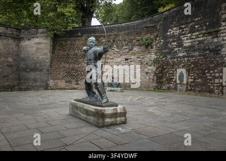 View of the bronze Robin Hood statue in a paved courtyard with a historic stone wall background in Nottingham, England, United Kingdom. Stock Photo
