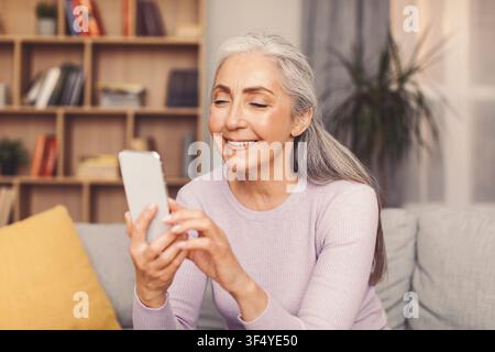 Happy Senior Woman Using Smartphone At Home, Technology Concept Stock Photo