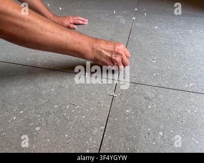 View of a worker installing grey ceramic floor tiles with plastic spacers in Riga, Latvia. Stock Photo