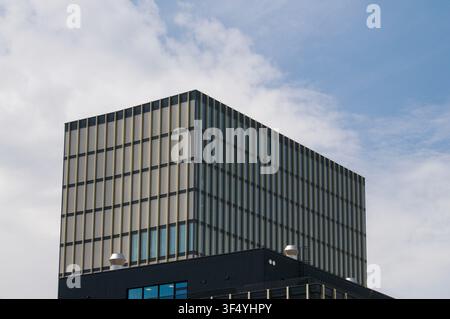 Low angle view of a modern office building featuring a minimalist facade with vertical golden slats and geometric grid structure under a blue sky Stock Photo