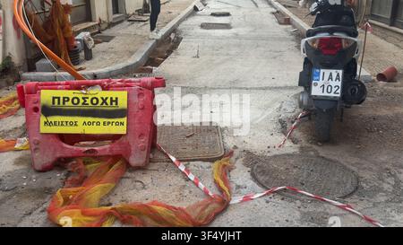 Red plastic barrier with Greek sign, safety tape and a parked scooter at a street construction site under repair that says "Closed due to construction Stock Photo