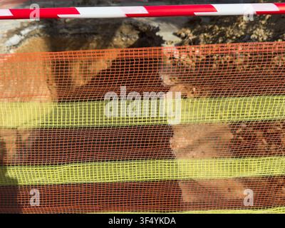 Macro-style detailed shot focusing on the texture of a synthetic orange and yellow striped safety mesh fence, partially revealing a construction pit. Stock Photo